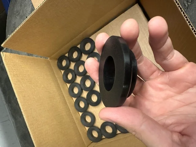 Rouleaux en polyuréthane noir à collerette dans une boîte d’expédition, un tenu en main montrant le profil moulé
